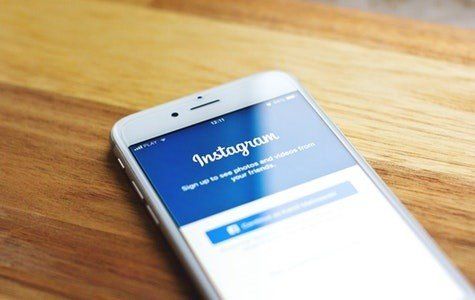 A white cell phone with the instagram app open on a wooden table.